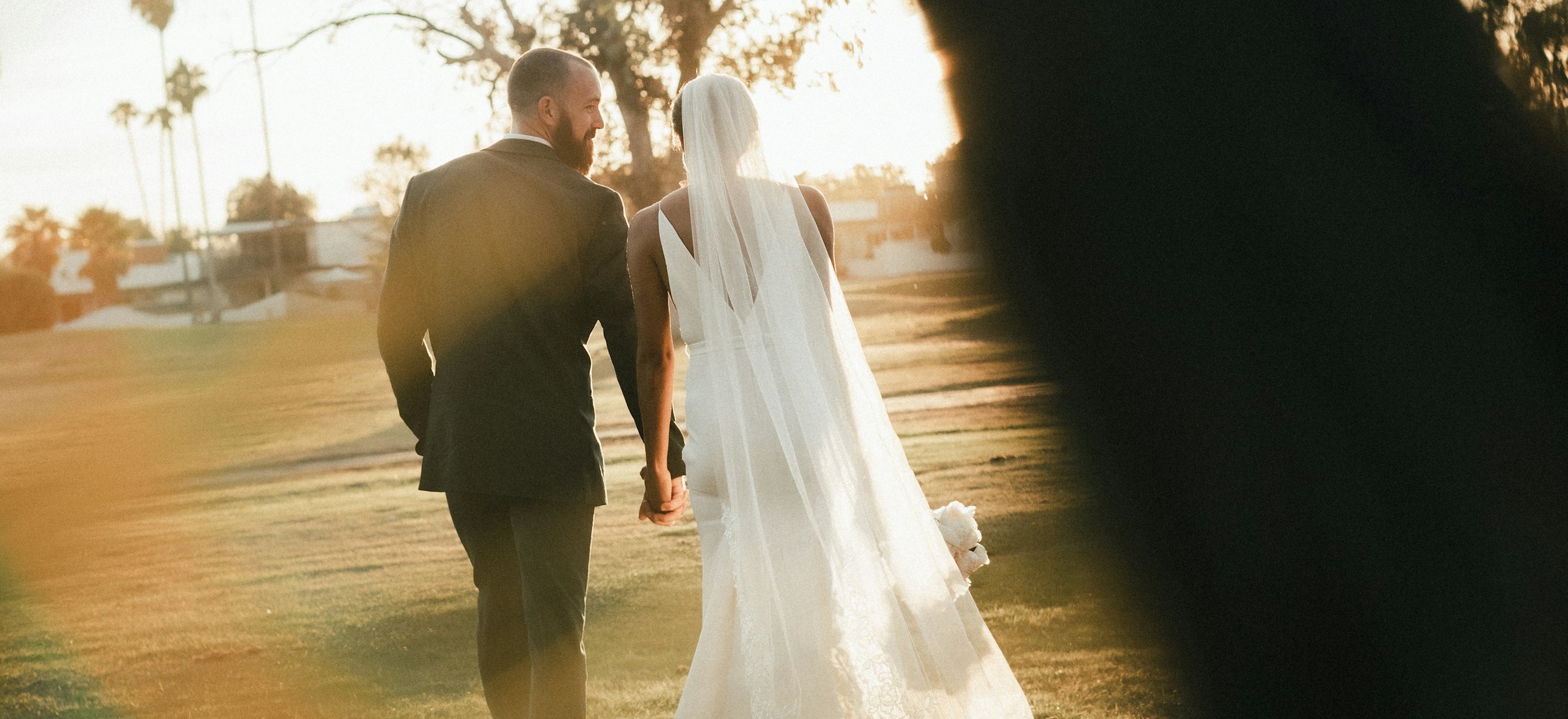 Bride and groom walking hand in hand across a sunlit lawn
